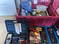 Overview of red plastic tote filled with electrical hardware and tools, multimeter case and wiring visible