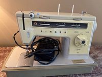 Front view of Singer sewing machine with controls, foot pedal and power cord on base