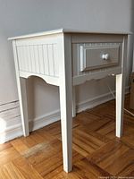 Angle view of white painted end table showing side paneling and drawer