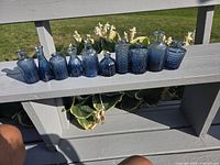 Row of 12 small blue glass bud vases on deck bench