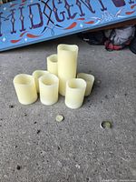 Seven ivory plastic flameless candles of varying heights on concrete surface