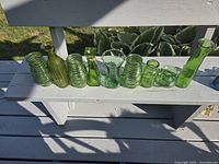 All eleven green glass vases lined on bench showing size range and designs