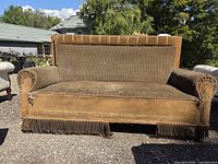 Front view of antique green-brown couch showing full design, fabric texture, rolled arms, fringe, and wear