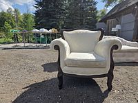 Front view of white upholstered armchair outdoors showing rolled arms and dark wood frame