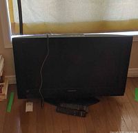 Front view of 32" Panasonic LCD TV on stand with two remotes