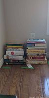 Two stacks of assorted cookbooks against wall