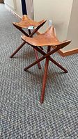 Pair of tripod stools side view showing leather seats and wooden legs