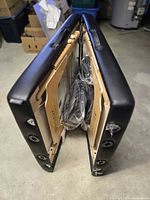 Folded massage table showing black vinyl exterior and wood interior with accessories inside