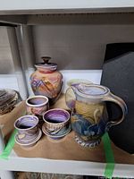 Shelf view showing lidded multicolour jar and small cream-plum vase among other pieces