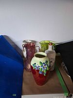 All four items grouped: ceramic vase, cranberry glass pitcher, lime glass pitcher, whisky bottle