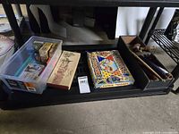 Shelf view showing plastic bin, board game boxes, game tin, and textile tools