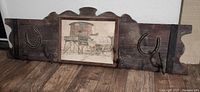 Full view of wood coat rack showing hooks, horseshoes and framed print