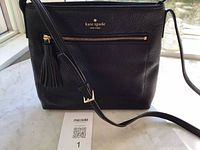 Front view of black Kate Spade purse showing tassel, front zip pocket, strap and label