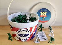 Bucket filled with green plastic soldiers, broken handle visible, lid and several figures displayed