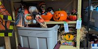 Shelf with multiple Halloween items including electric jack-o-lantern, witch, pumpkins, storage tote