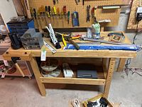 Front view of wooden workbench showing vise clamp, top tray, and pegboard tools (contents not included)