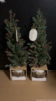 Two boxed faux evergreen trees with red berries and ceramic pots