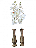 Two tall engraved brass vases with white orchid stems