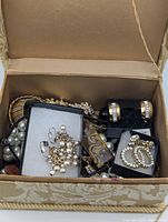 Open fabric jewelry box showing assorted necklaces, bracelet, brooches and earring sets
