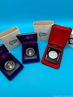 Wide shot showing three cased commemorative dollars with their outer boxes