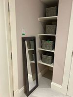 Mirror leaning against wall and four wicker baskets on shelves