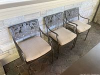 Three cast iron patio chairs with cushions against wall
