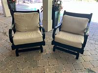 Front view of both matching black metal rocking chairs with beige cushions on patio