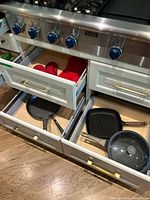 Open drawers showing grill pan, non-stick fry pan with glass lid and red oven mitts