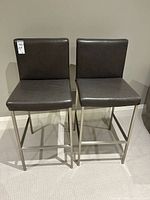 Front view of both stools showing leather upholstery and metal frames