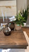 Tabletop view of both glass vases and peace lily plant in basket