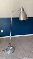 Full view of silver floor lamp standing upright, base to shade