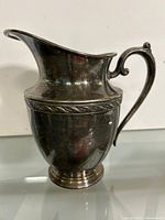 Front view of silverplate pitcher showing shape, handle, decorative band and pedestal base