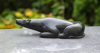 Front-left view of reclining soapstone polar bear sculpture on stone surface