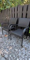 Pair of brown synthetic rattan arm chairs on gravel