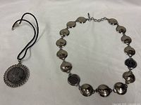 Both necklaces laid flat: coin-link Buffalo nickel necklace and leather cord pendant