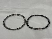 Both sterling silver bracelets lying flat showing overall form and clasps