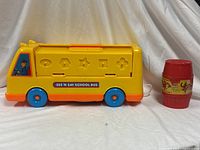 Left side view of yellow See 'n Say School Bus toy with shape cut-outs and red Barrel of Monkeys beside it
