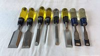 Eight chisels and scrapers arranged side by side showing blades and handles