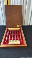 Open presentation box showing six stainless steel steak knives seated in red velvet insert