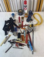 Full view of assorted tools, brushes, cords, tape and accessories on white surface