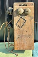 Front view of wooden Western Electric wall telephone showing bells, handset, cord, crank and missing transmitter