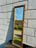 Full view of gilded rectangular mirror leaning against wall