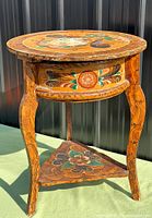 Full view of round lift-top table showing painted top, curved legs and lower shelf