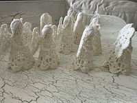 Seven of the nine white crochet angel ornaments displayed upright on a distressed white surface