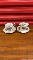 Pair of Royal Albert Flower of the Month teacup and saucer sets displayed side by side