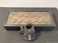 Top view showing wood box lid with ten coins and padlock in foreground