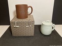Brown clay mug on patterned box beside celadon mug
