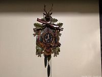 Full view of hanging cuckoo clock with stag head, rifle, leaves, weights visible