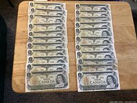 Fronts of 22 Canadian $1 bills laid out in two rows on table