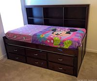 Full view of trundle bed showing bookcase headboard, drawers, and fitted sheet
